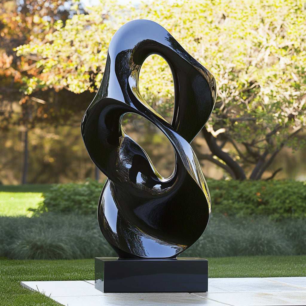 Modern abstract polished black outdoor sculpture with flowing curves, displayed on a black base in a landscaped garden setting.