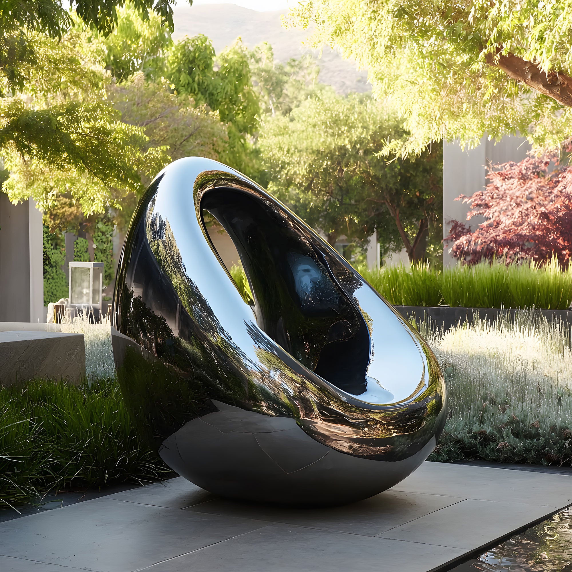 Modern stainless steel mirror finish sculpture in a garden setting with trees and grass.