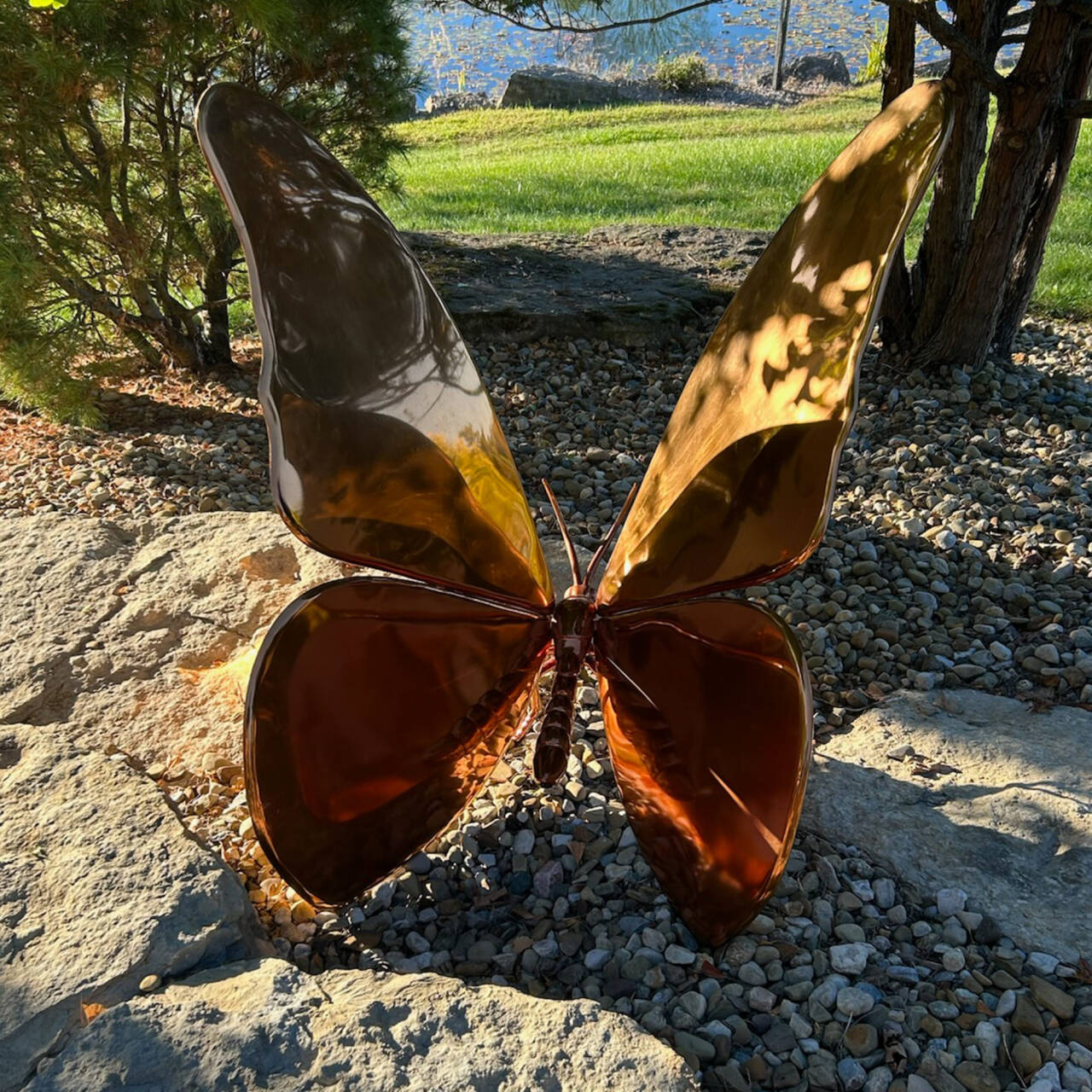 Custom stainless steel butterfly sculpture with brass electroplated mirror finish, created specifically for Schnormeier Gardens in Gambier, Ohio, integrated into a natural stone garden setting