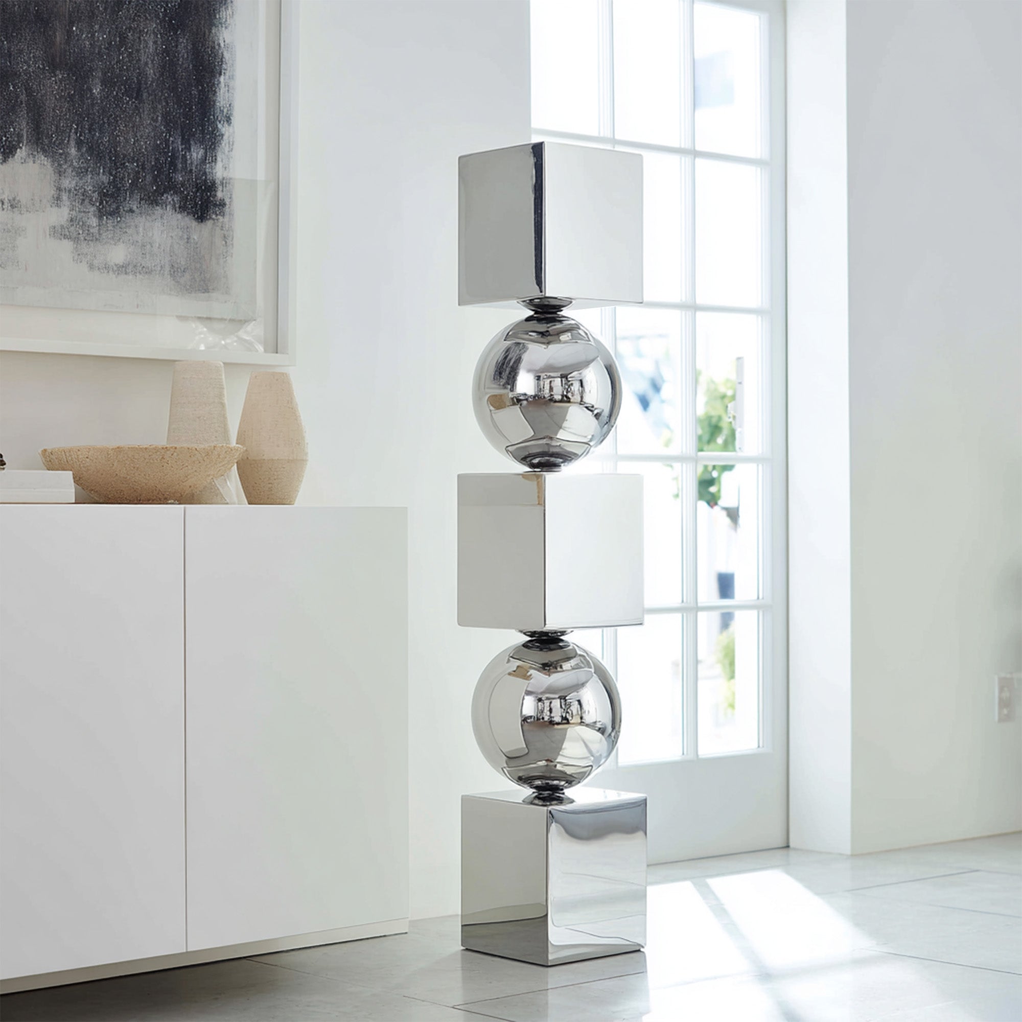 Modern stainless steel polished sculpture in a bright room with large windows.